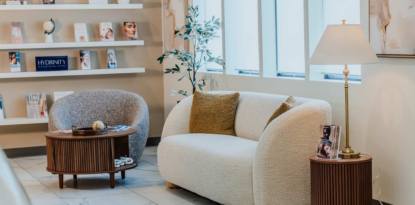 The Clinique La Roya waiting lounge: a boucle sofa and armchair, product shelves, and a window wall