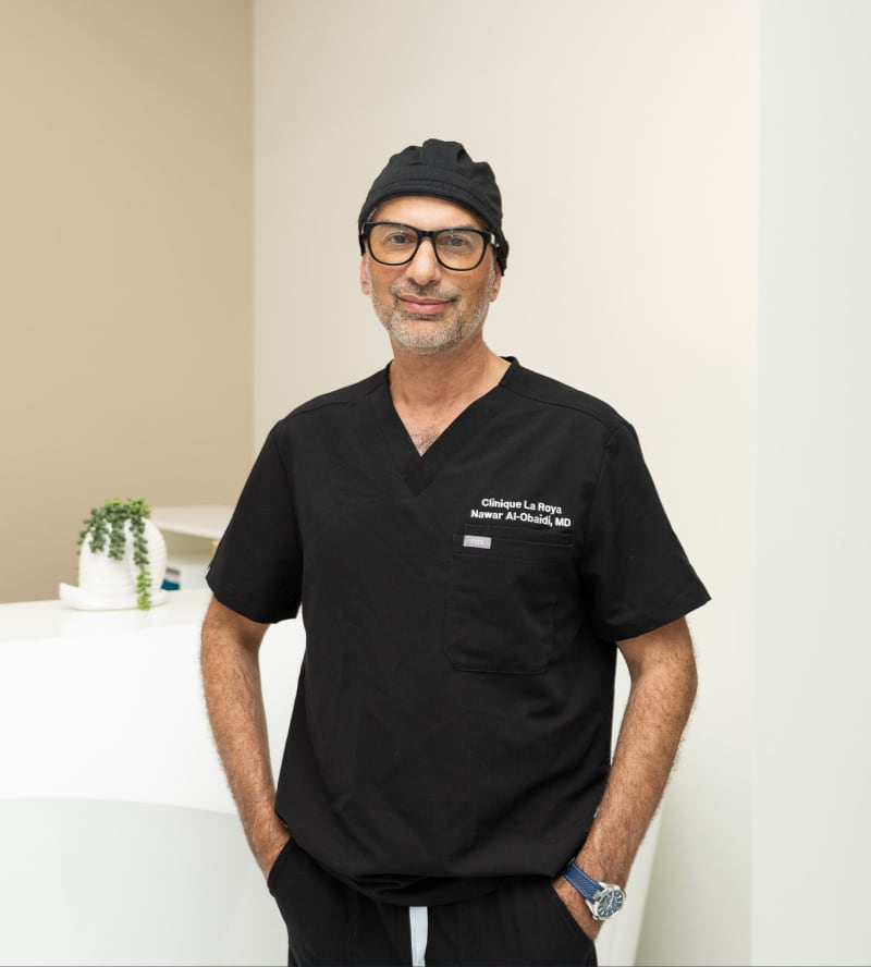 Dr. Nawar Al-Obaidi, MD, standing in black Clinique La Roya scrubs at the clinic reception desk