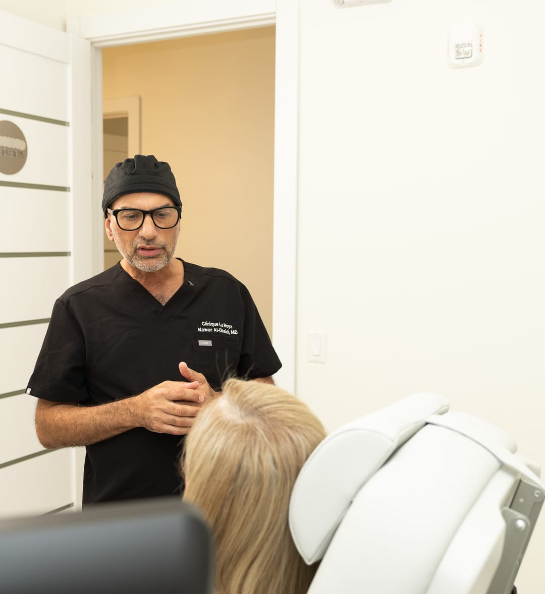 Dr. Nawar Al-Obaidi talking with a seated patient at Clinique La Roya