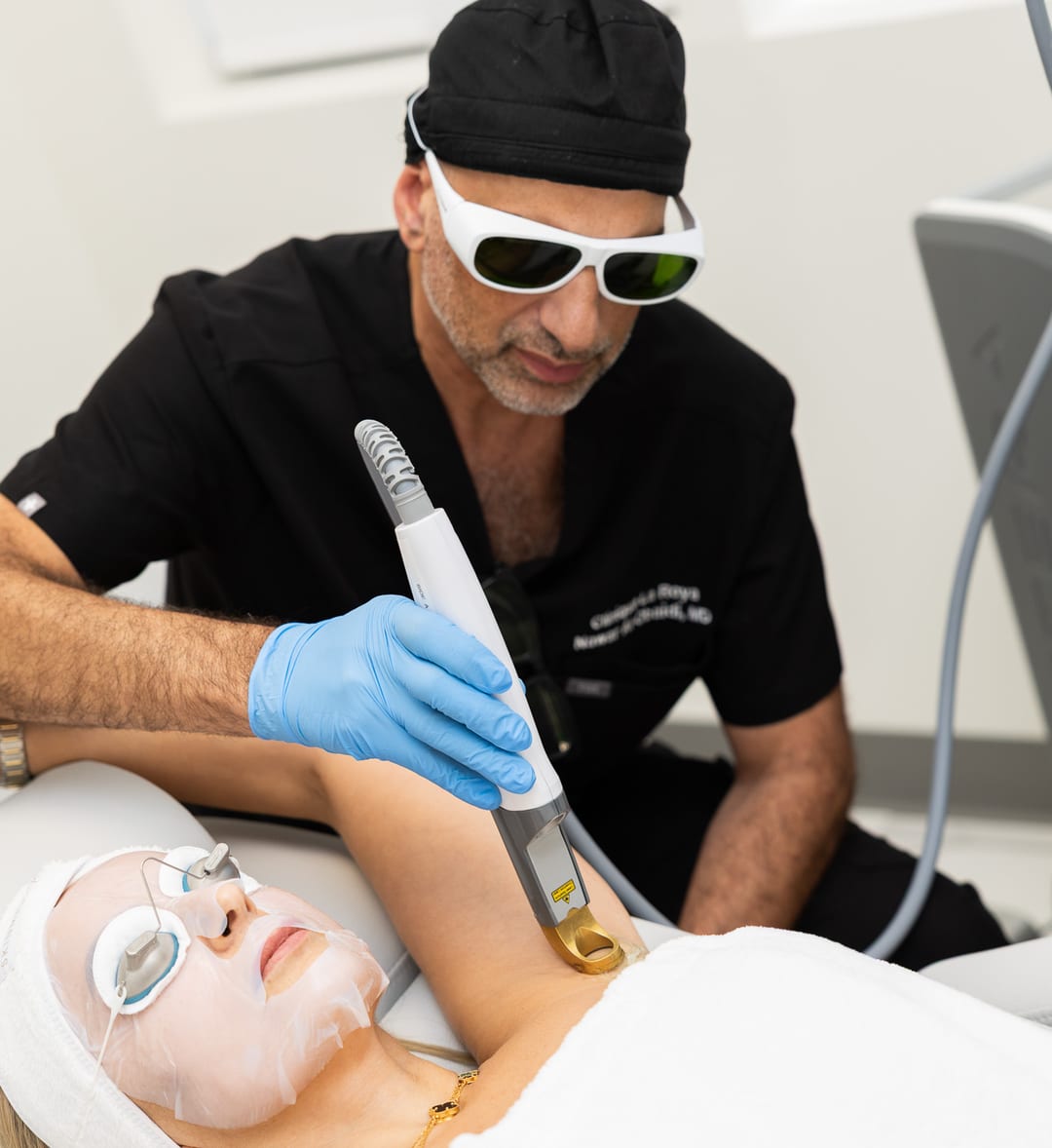 Dr. Nawar Al-Obaidi, wearing protective goggles, treating a patient’s face with a laser handpiece