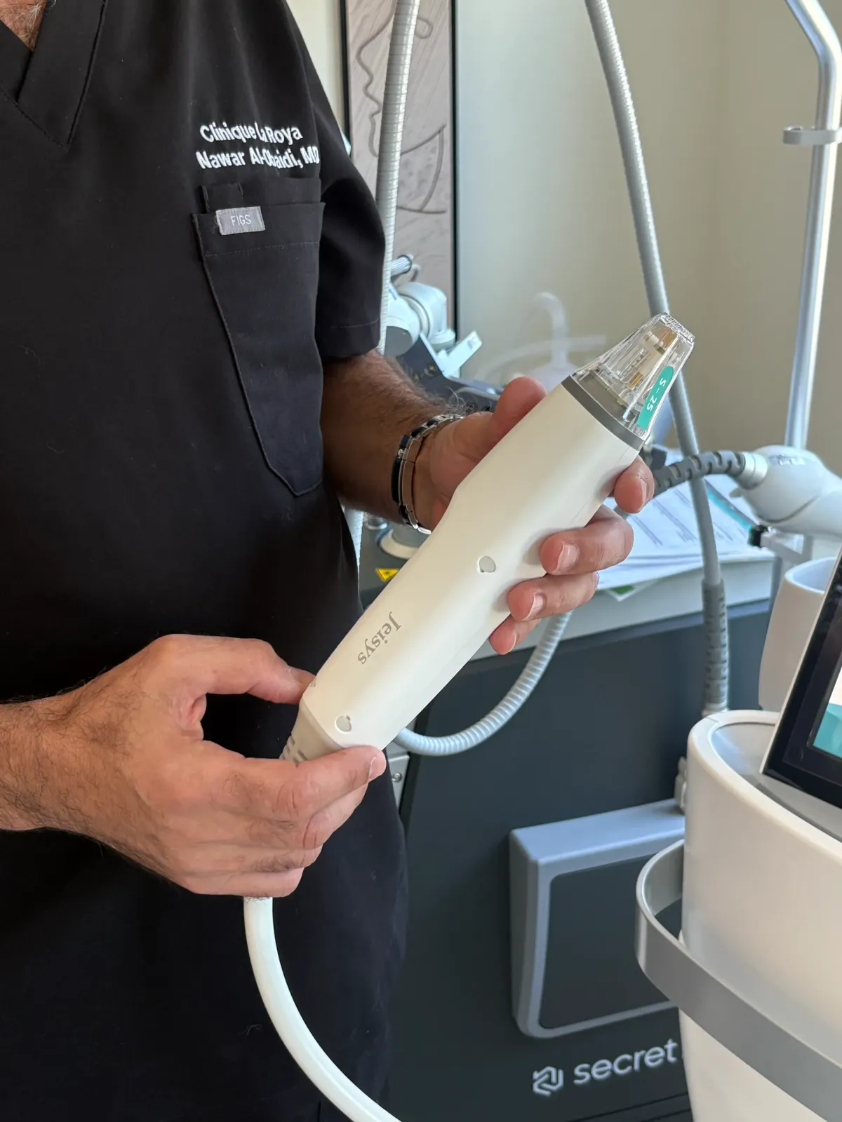 A physician holding a microneedling handpiece beside the treatment device