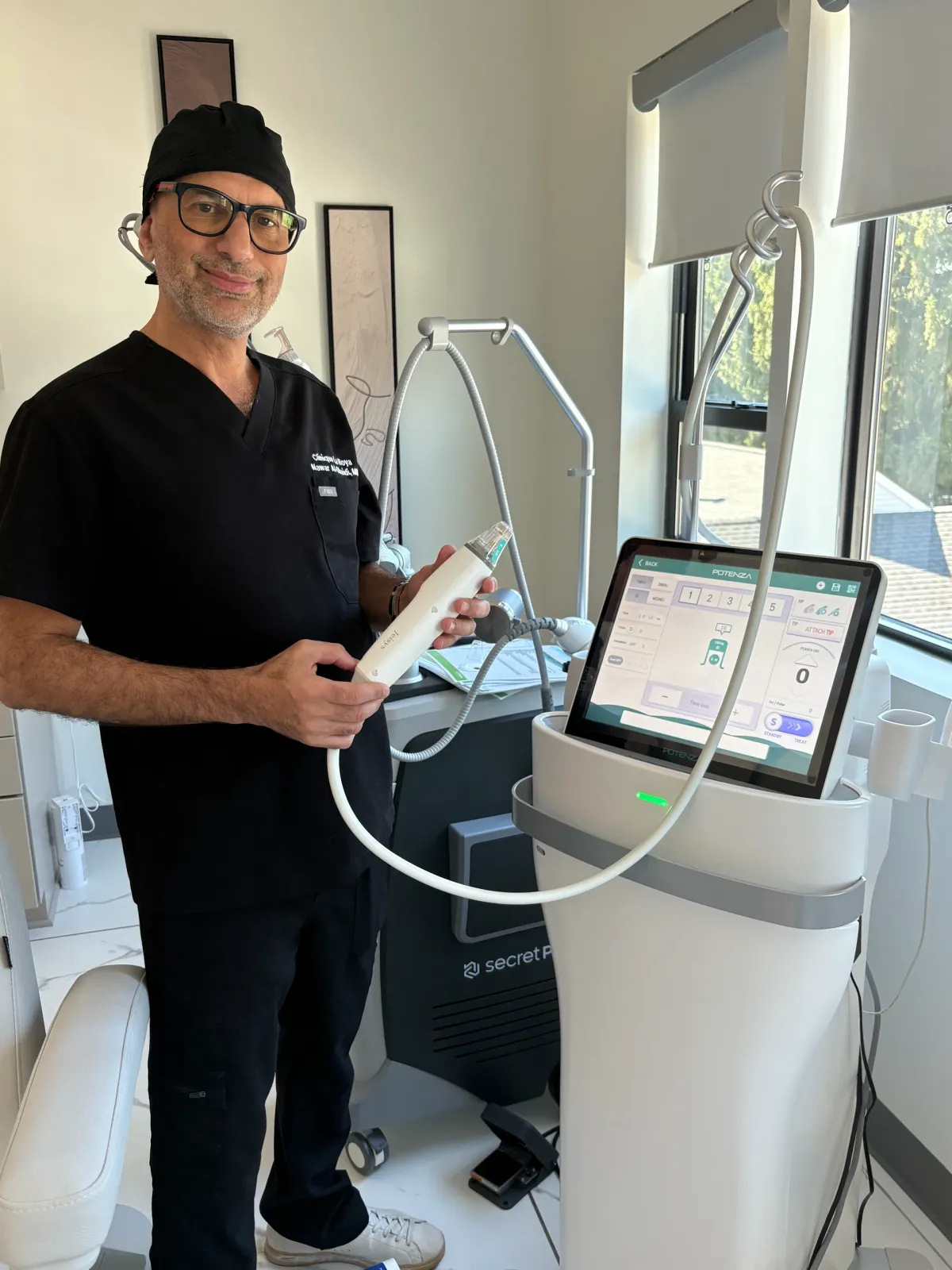 Dr. Nawar Al-Obaidi holding a microneedling handpiece beside the treatment device at Clinique La Roya